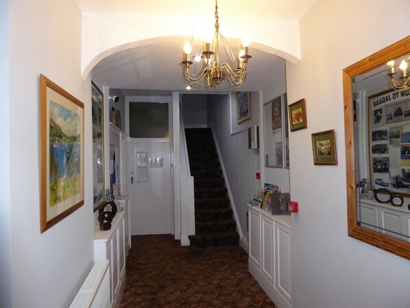 A hallway with a staircase, framed pictures, and a chandelier. - The Berwick - Over 40's Only (Blackpool)