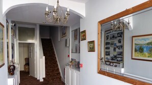 Een hal met patroonloos tapijt, een trap, een kroonluchter, ingelijste foto's en een spiegel die een landschaps schilderij weerspiegelt.