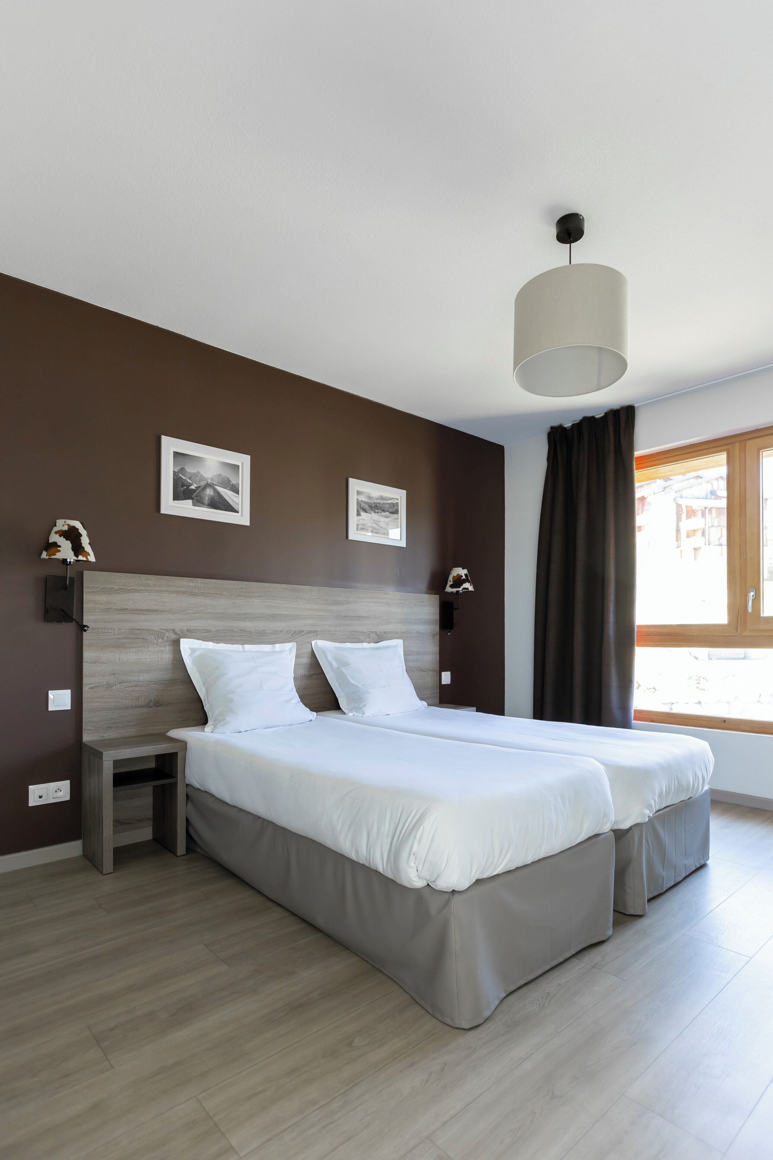 A double bed with a wooden headboard, a bedside table, a wall-mounted lamp, and two framed pictures on the wall.