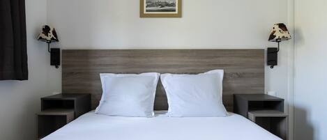Una cama bien hecha con sábanas blancas, dos mesitas de noche, un cabecero y dos lámparas de pared con pantallas de cuero.
