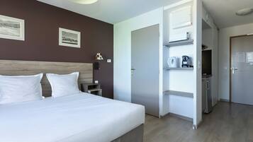Una habitación de hotel con cama, armario, escritorio y kitchenette.