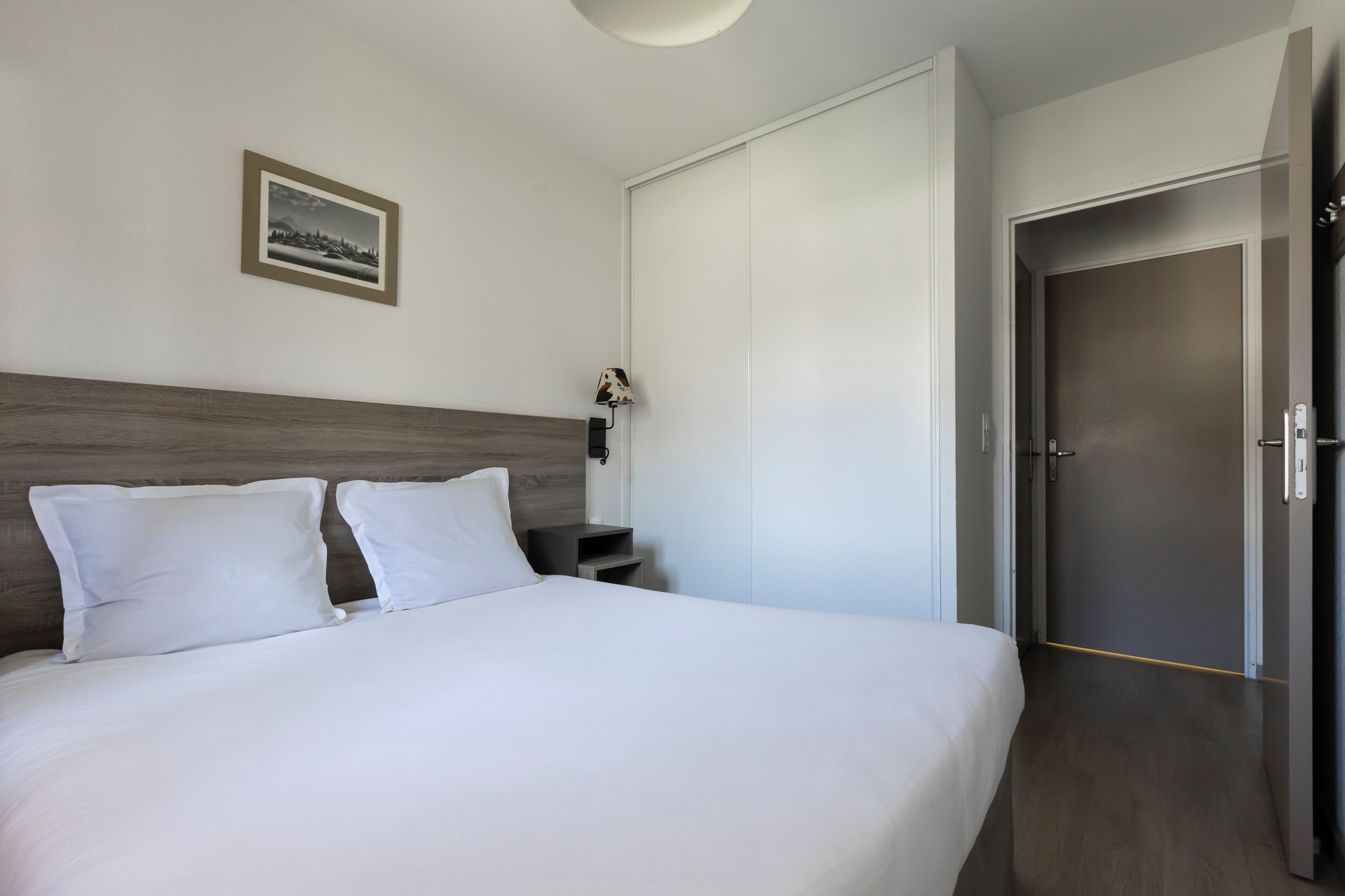 Habitación de hotel con una cama grande, una mesita de noche, una lámpara, un armario y una puerta.