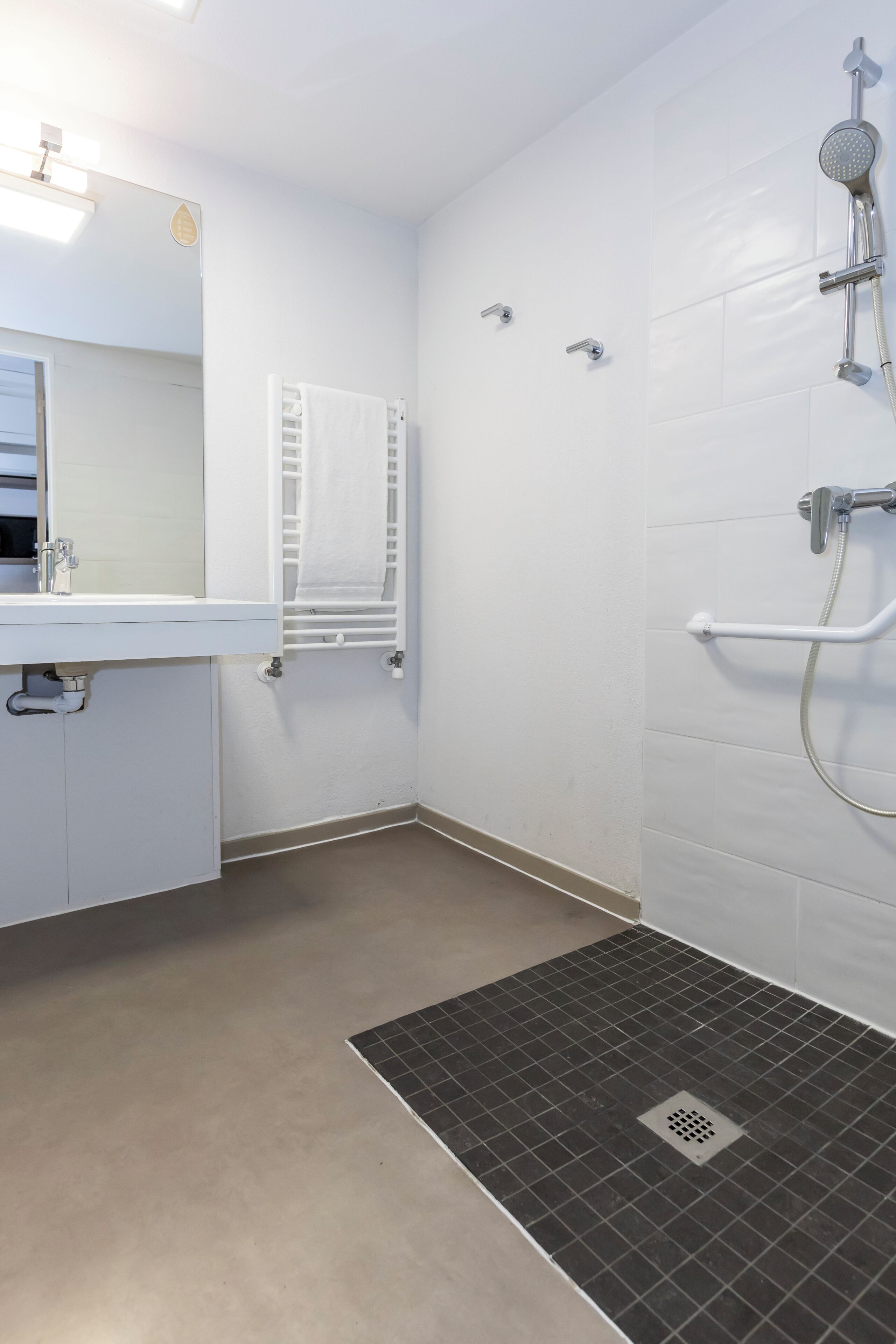 Een badkamer met een witte wastafel, spiegel, handdoekrek, douche en afvoerrooster.