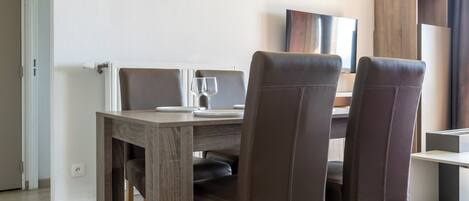 A dining area with a wooden table, two chairs, a hanging light fixture, and a framed picture on the wall.