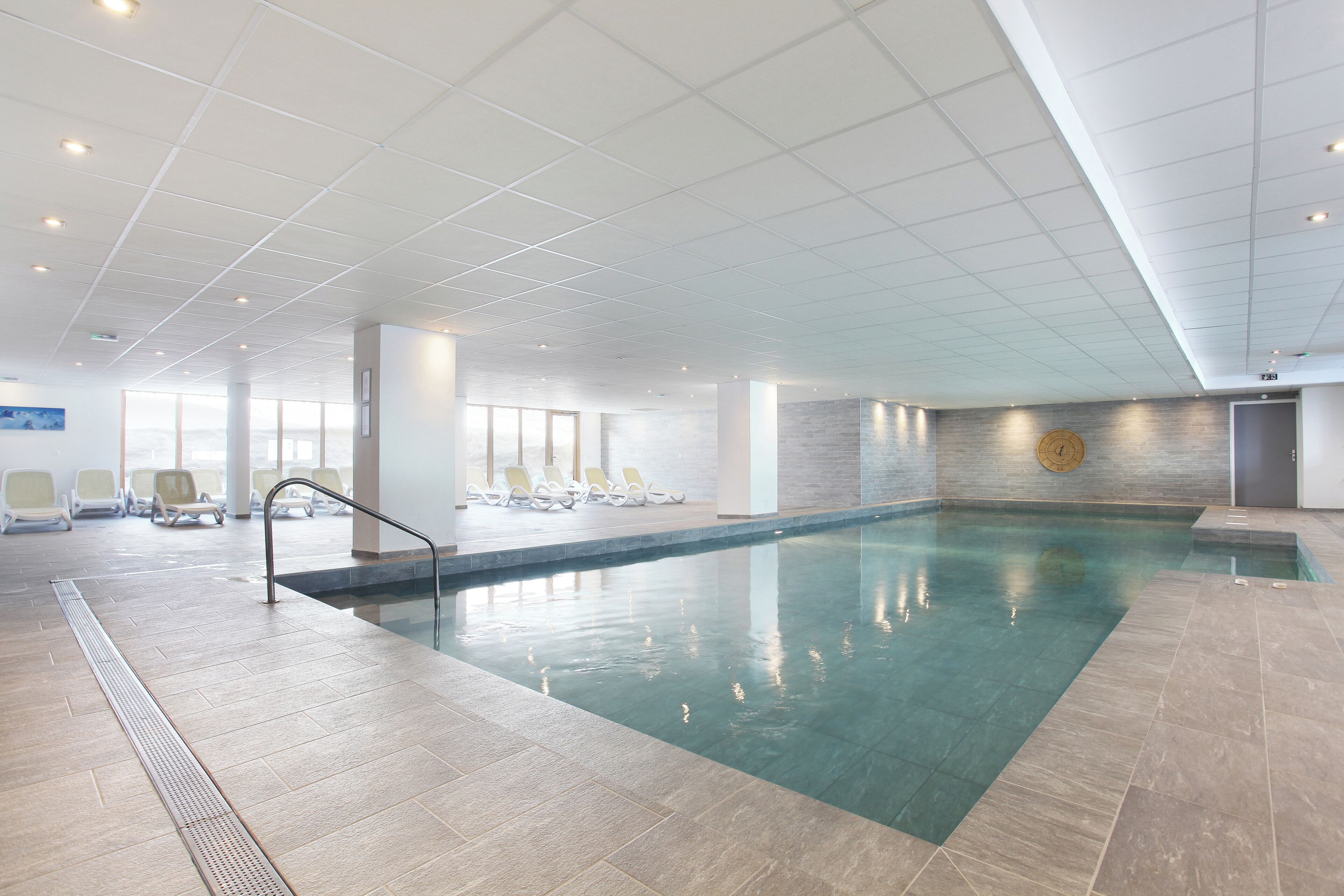 An indoor swimming pool with clear water, a tiled floor, and a ceiling with recessed lighting.