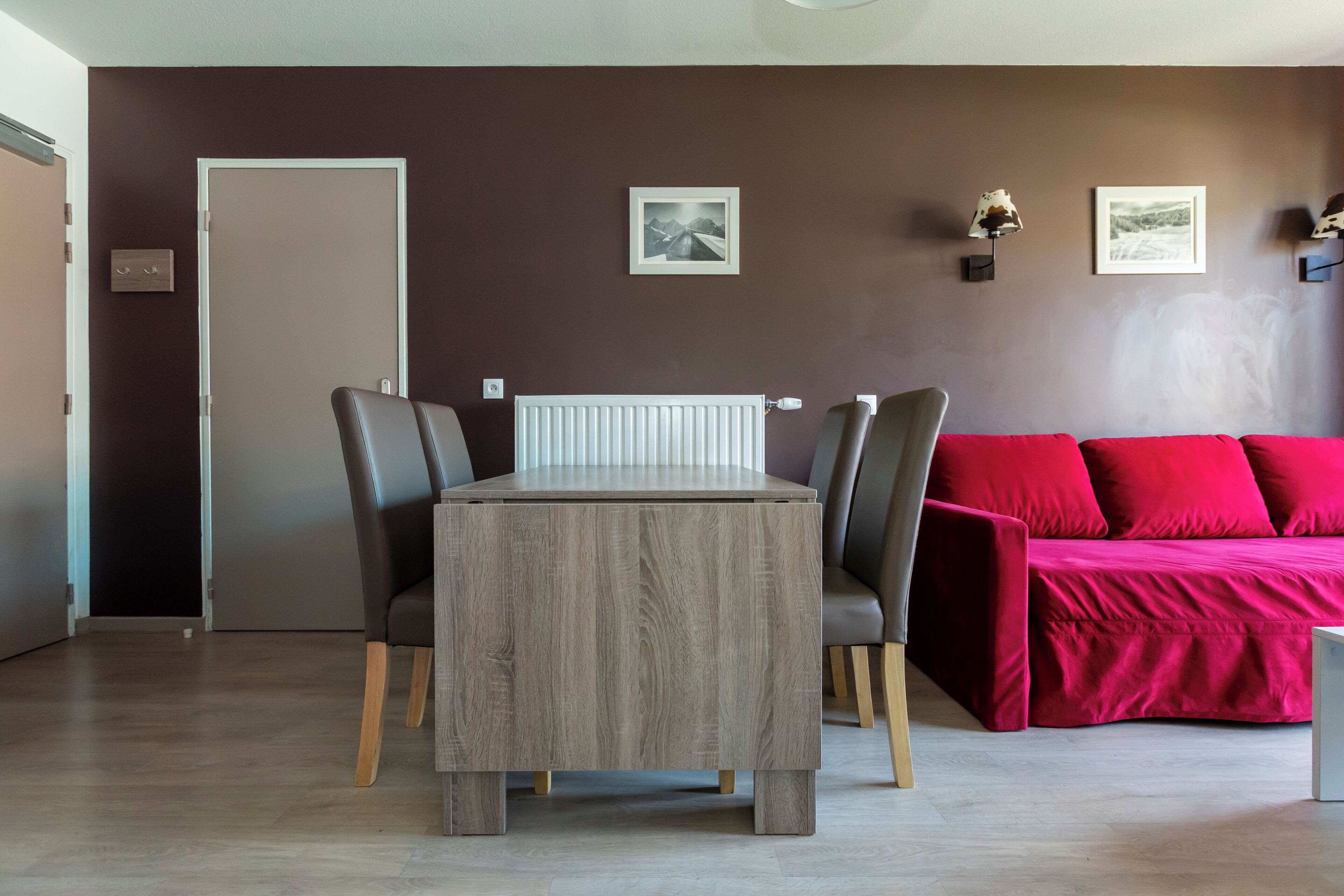 Een moderne woonkamer met een eettafel, twee stoelen, een rode bank en een radiator.