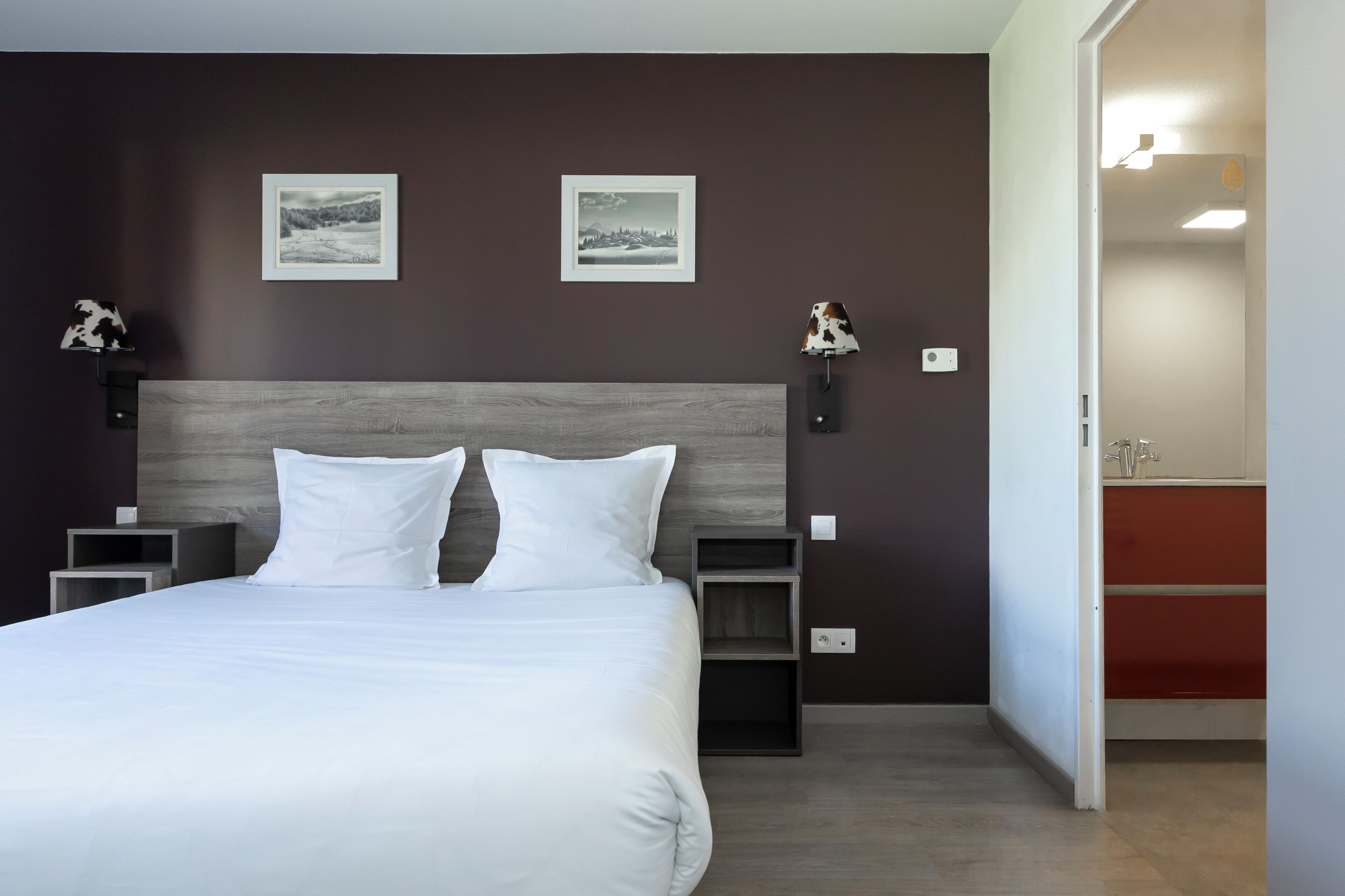 A neatly made bed with a wooden headboard, two bedside tables, and two wall-mounted lamps.