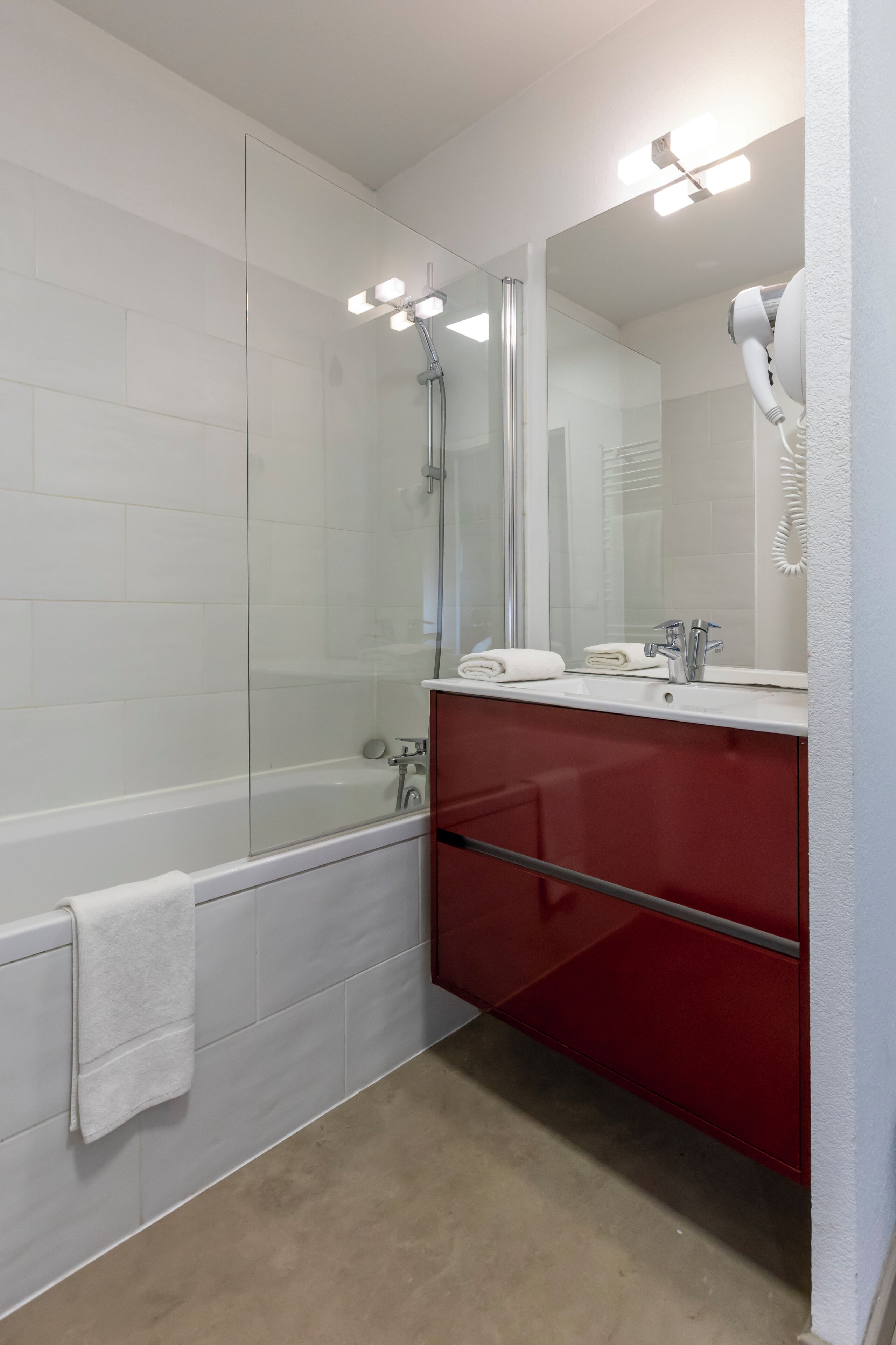 A modern bathroom with a glass shower enclosure, a white bathtub, a red vanity, and a large mirror.