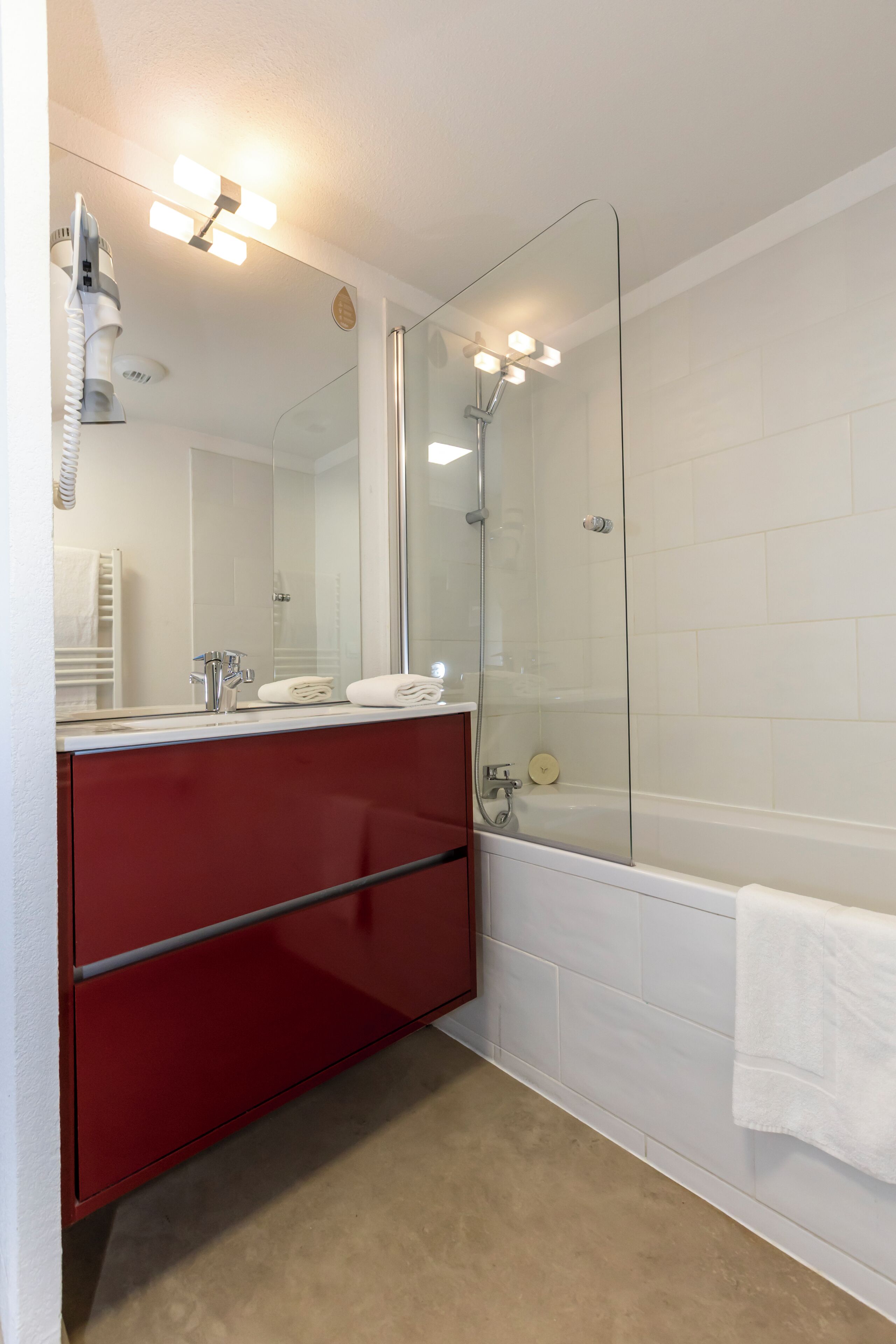 Een badkamer met een douche in een glazen cabine, een rode wastafel, een wit bad en een grote spiegel met verlichting.