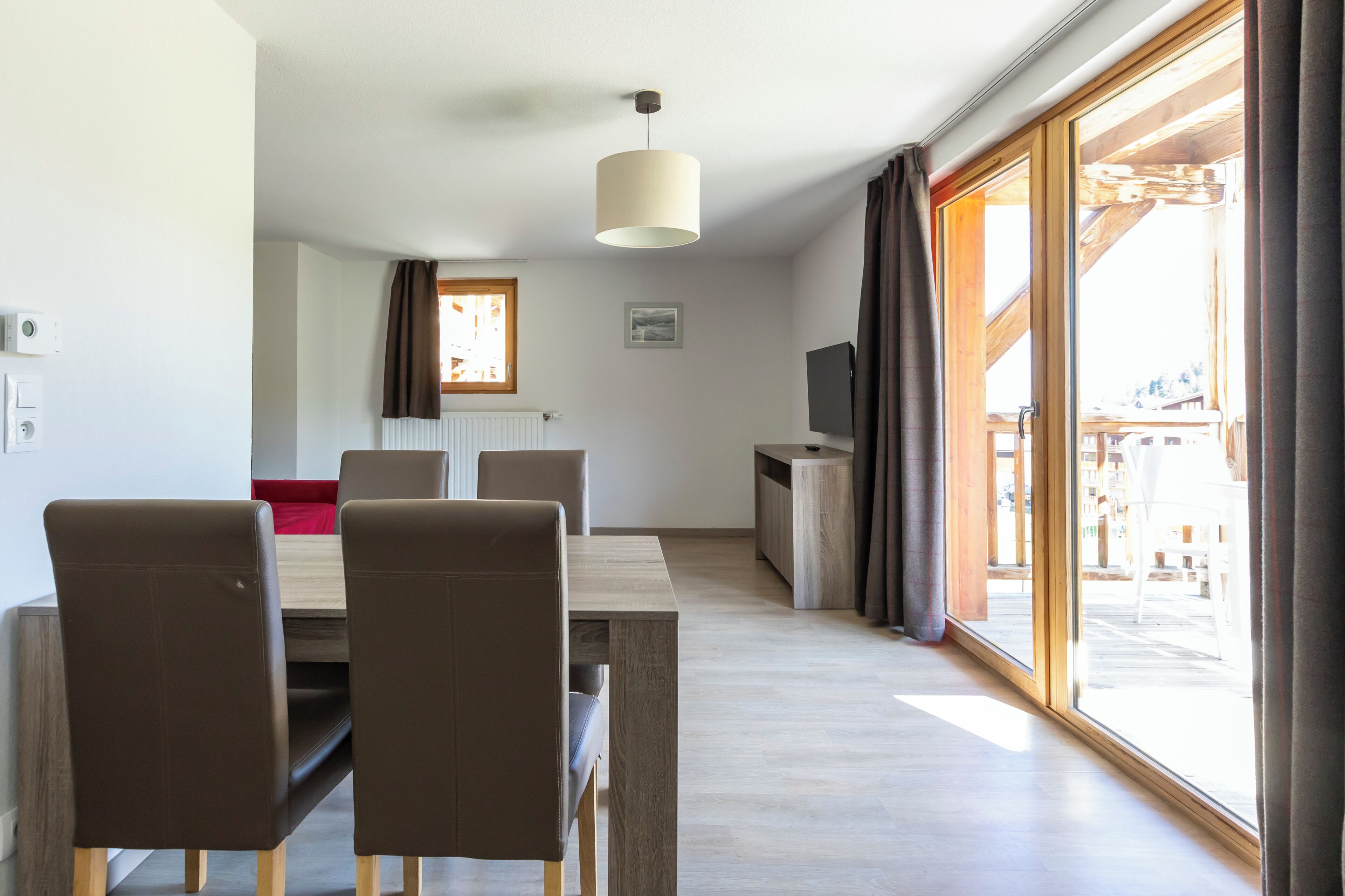 Een moderne kamer met een eethoek, een televisie en een groot raam met gordijnen.