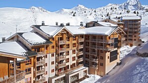 Una cabaña de madera de varios pisos con balcones, frente a un paisaje montañoso nevado.