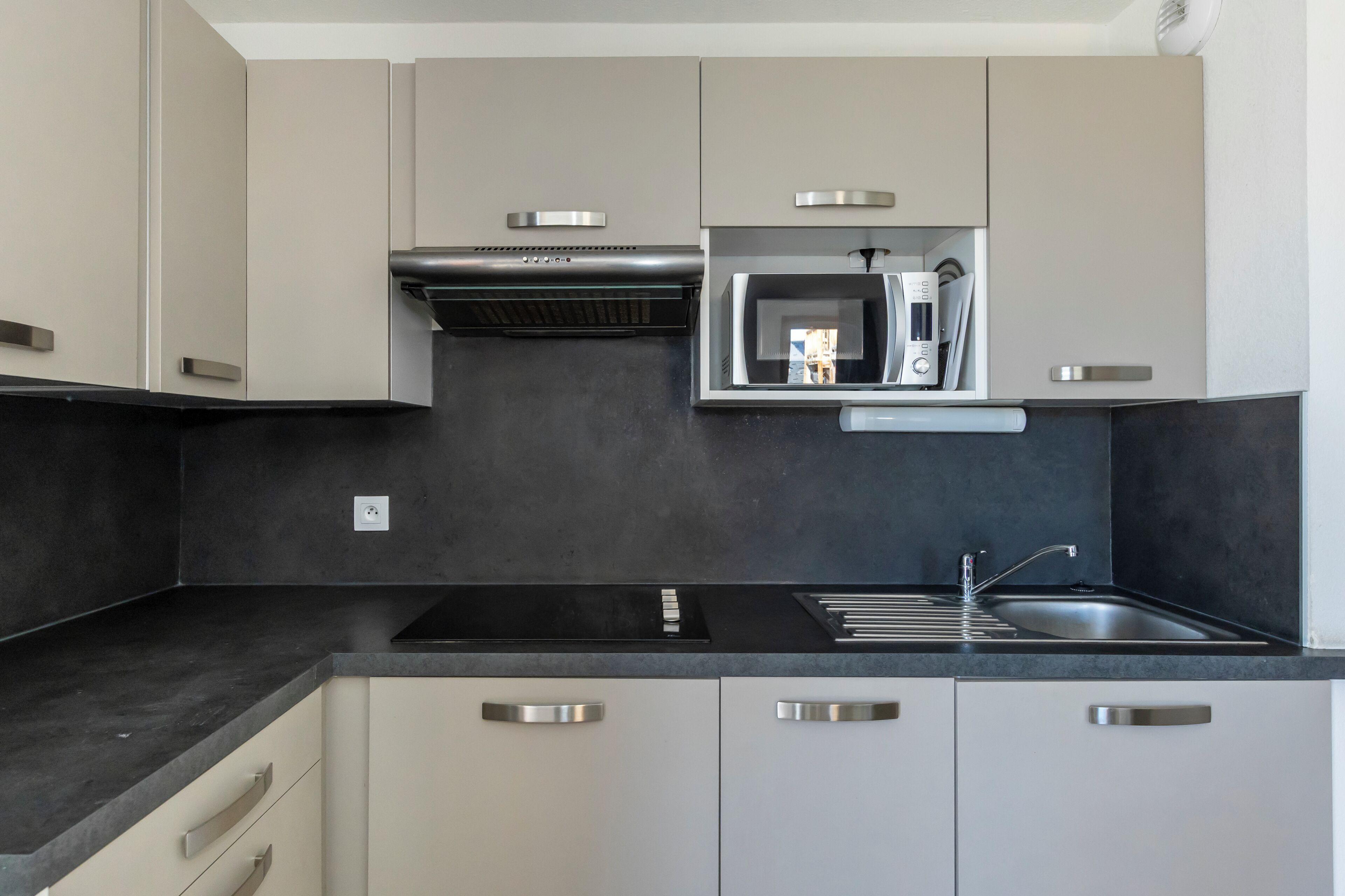 A modern kitchen with a built-in microwave, stainless steel appliances, and a black countertop.