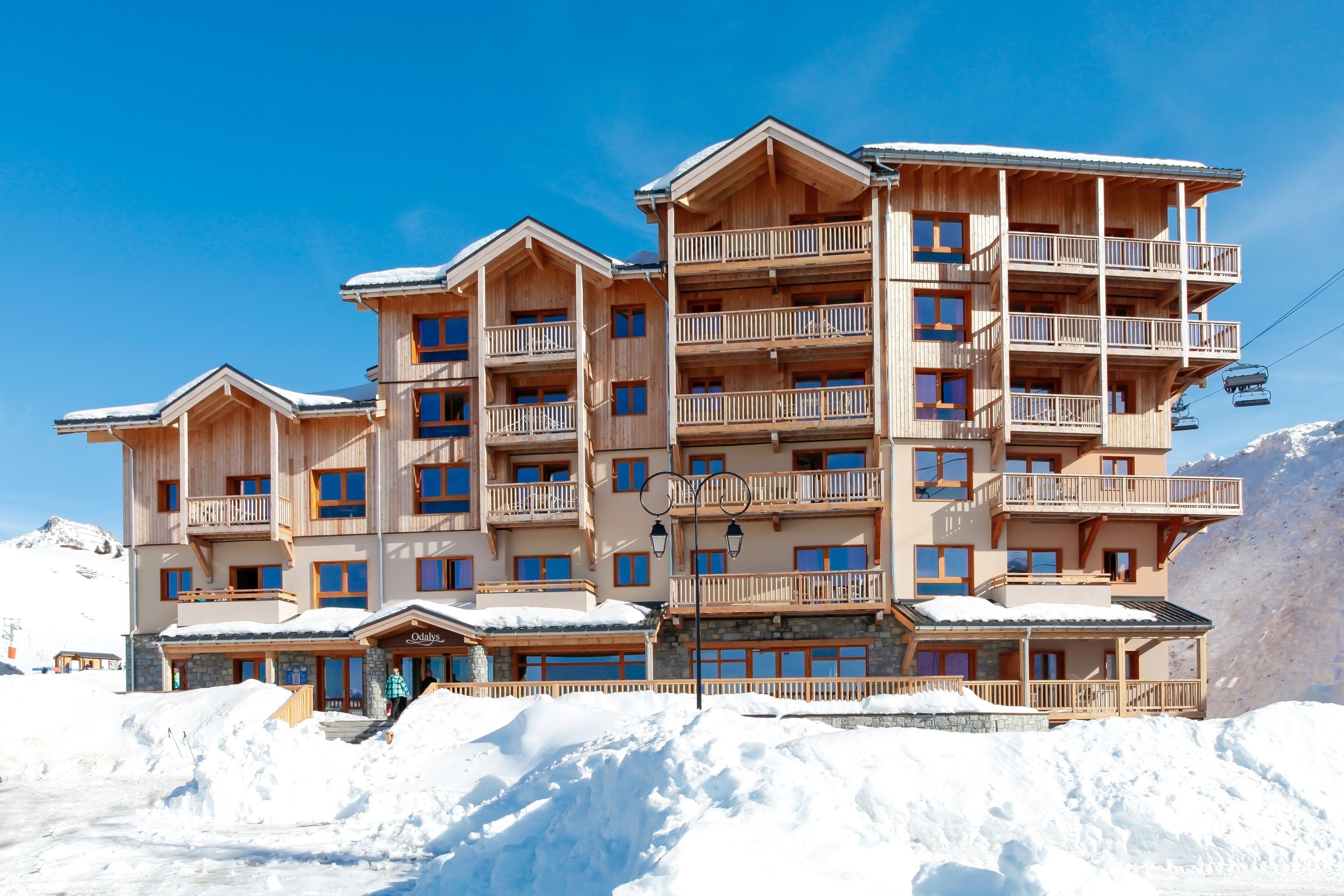 A multi-story wooden hotel with balconies, a ski lift, and snow-covered surroundings.