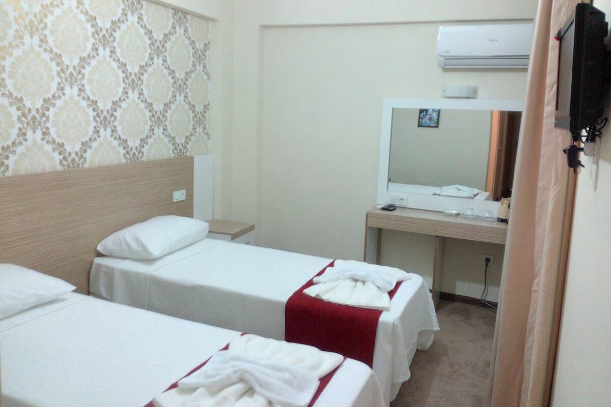 Habitación de hotel con dos camas individuales, un escritorio con espejo y un equipo de aire acondicionado en la pared.