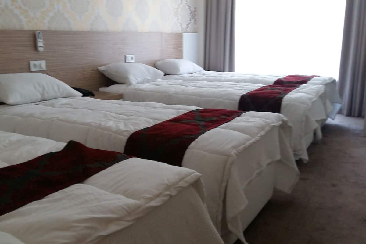 Habitación de hotel con tres camas individuales, cada una con ropa blanca y una manta roja. Las camas están alineadas contra una pared con cabecera de madera.