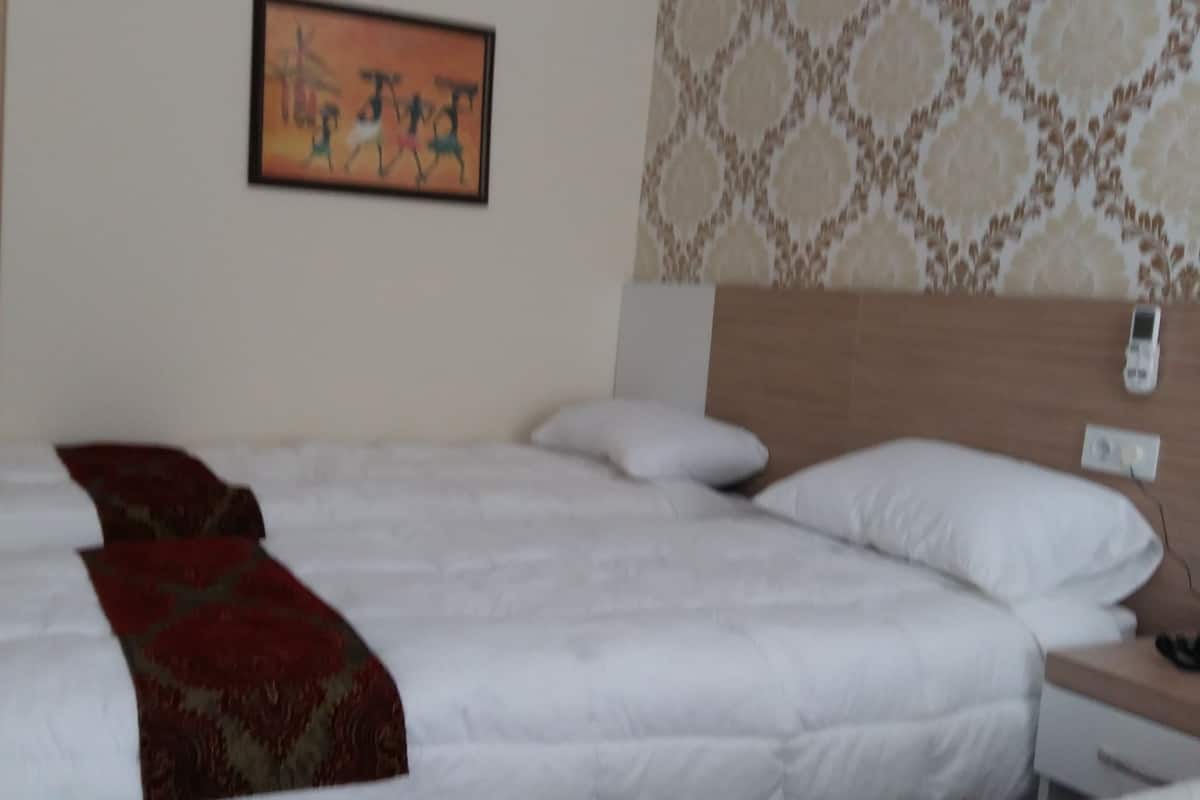 Habitación de hotel con una cama grande, una mesita de noche, un teléfono en la pared y un papel tapiz estampado.