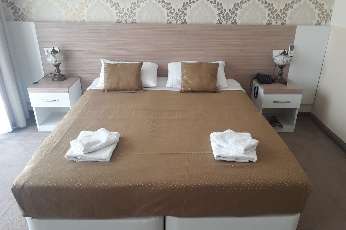 Una habitación de hotel con una cama grande, dos mesitas de noche, una lámpara de noche y un teléfono.