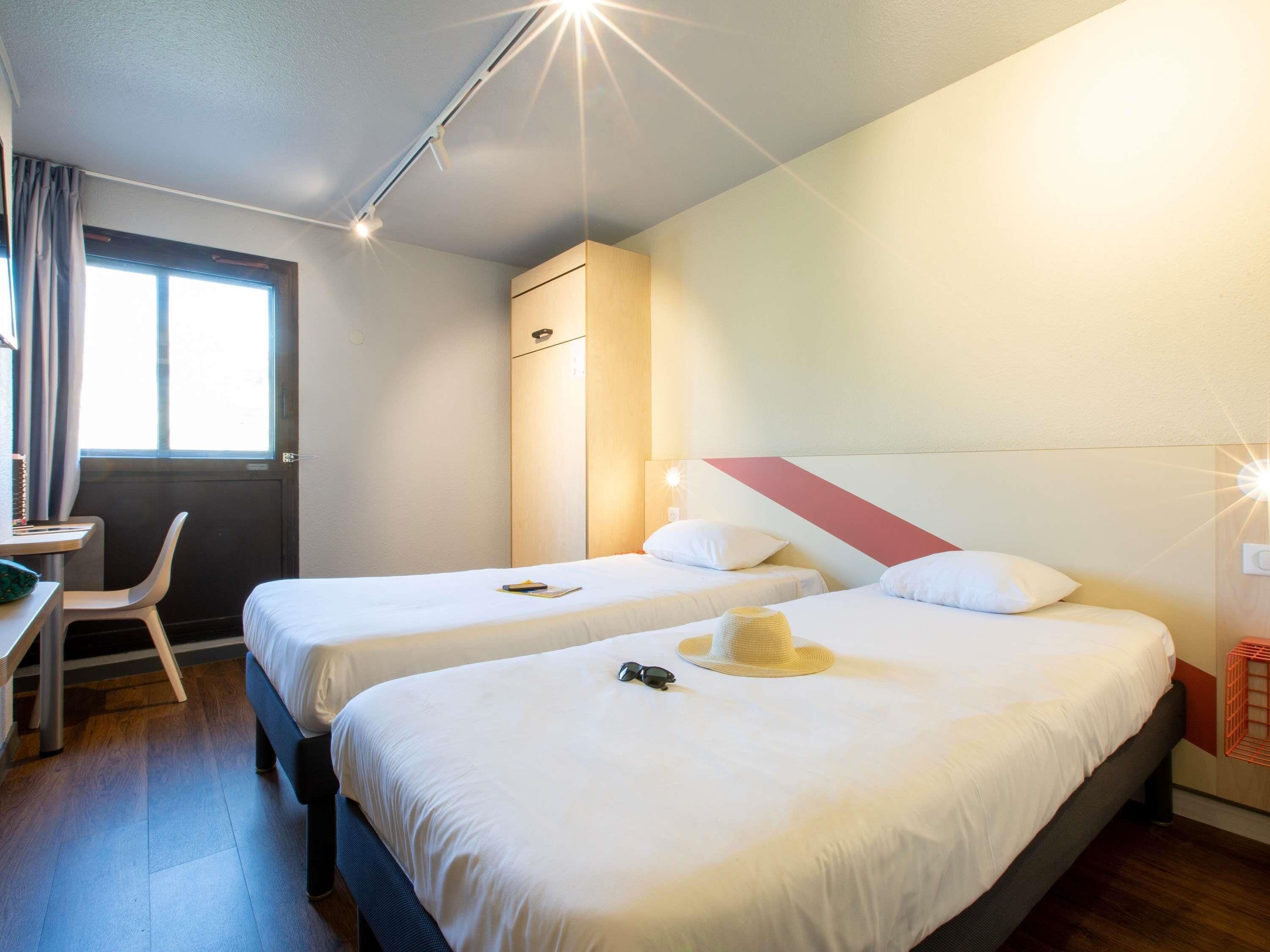 A hotel room with two beds, a desk, a chair, and a window.