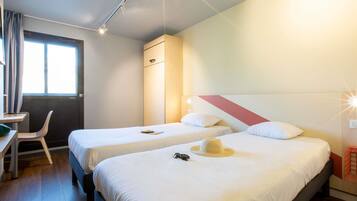 A hotel room with two beds, a desk, a chair, and a window.