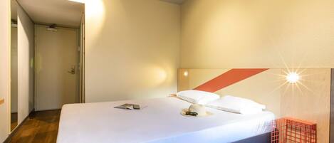 Une chambre d’hôtel moderne avec un grand lit, un plancher en bois, une porte et un luminaire fixé au mur.