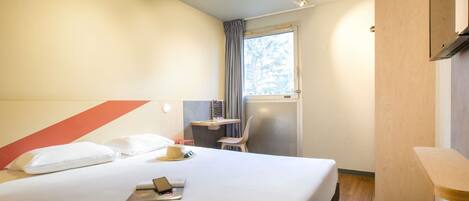 A hotel room with a bed, a desk, a chair, and a window with curtains.