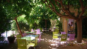 An outdoor seating area with tables and chairs under trees, surrounded by greenery.