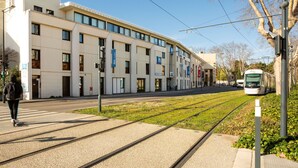 A modern building with multiple windows and a tram line running alongside it.