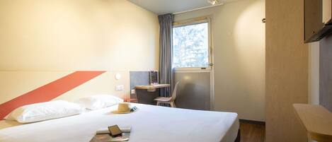 A hotel room with a bed, a desk, a chair, a window, and a mirror.