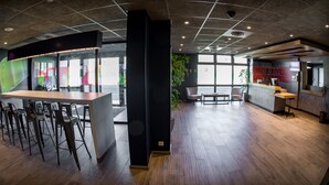 A modern office space with a long wooden table and bar stools, a large window, and a reception area with a counter and chairs.