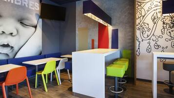 Un interior de restaurante moderno con asientos coloridos, una zona de bar central y un gran mural en la pared.