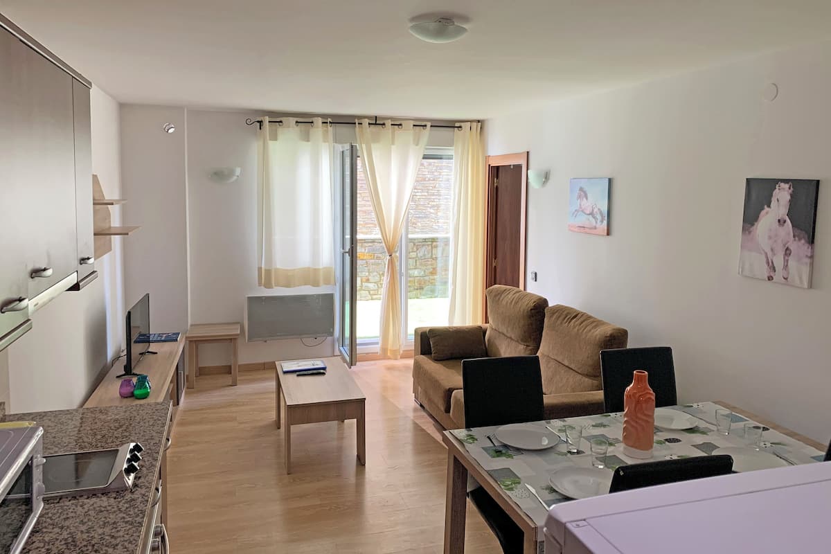 Uma sala de estar moderna com sofá, uma mesa de jantar posta para dois e uma cozinha com fogão e micro-ondas.