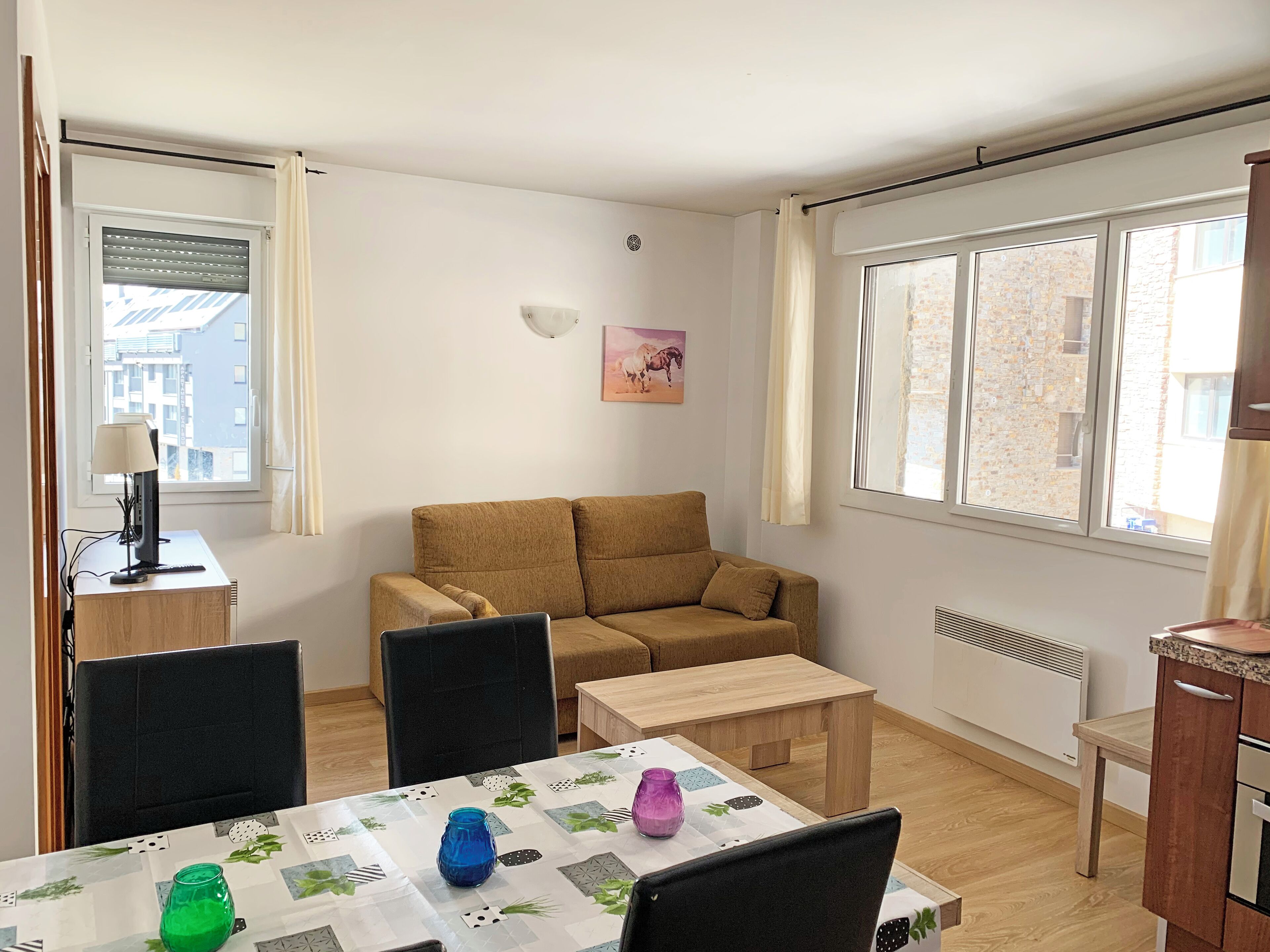 Una sala de estar acogedora con un sofá, una mesa de comedor con sillas, una lámpara y una ventana con cortinas.