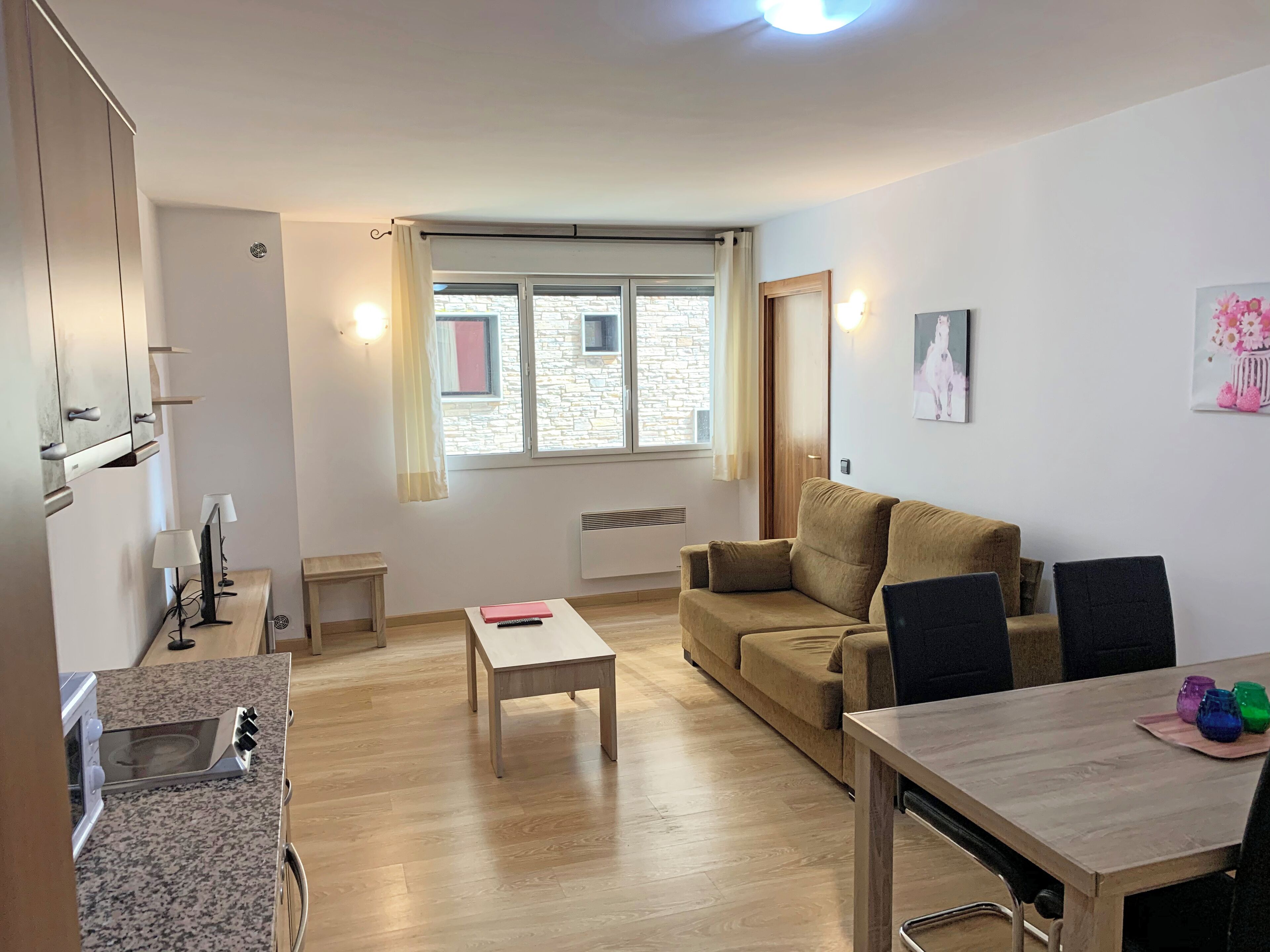 A compact living space with a kitchenette, a sofa, a dining table, and a window with curtains.