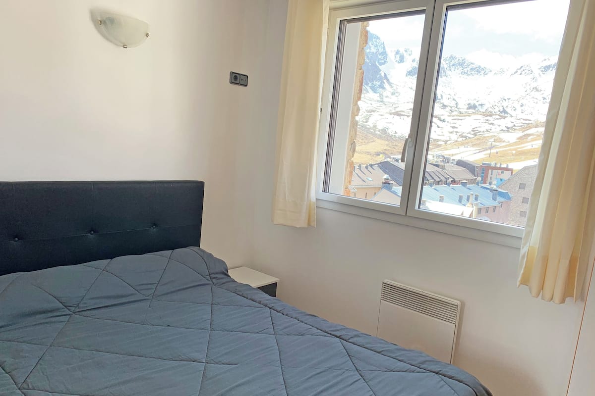 Quarto com cama grande, janela com vista para montanhas, luminária na parede e termostato.