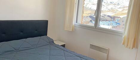 Une chambre avec un grand lit, une fenêtre donnant sur les montagnes, une lampe fixée au mur et un thermostat.