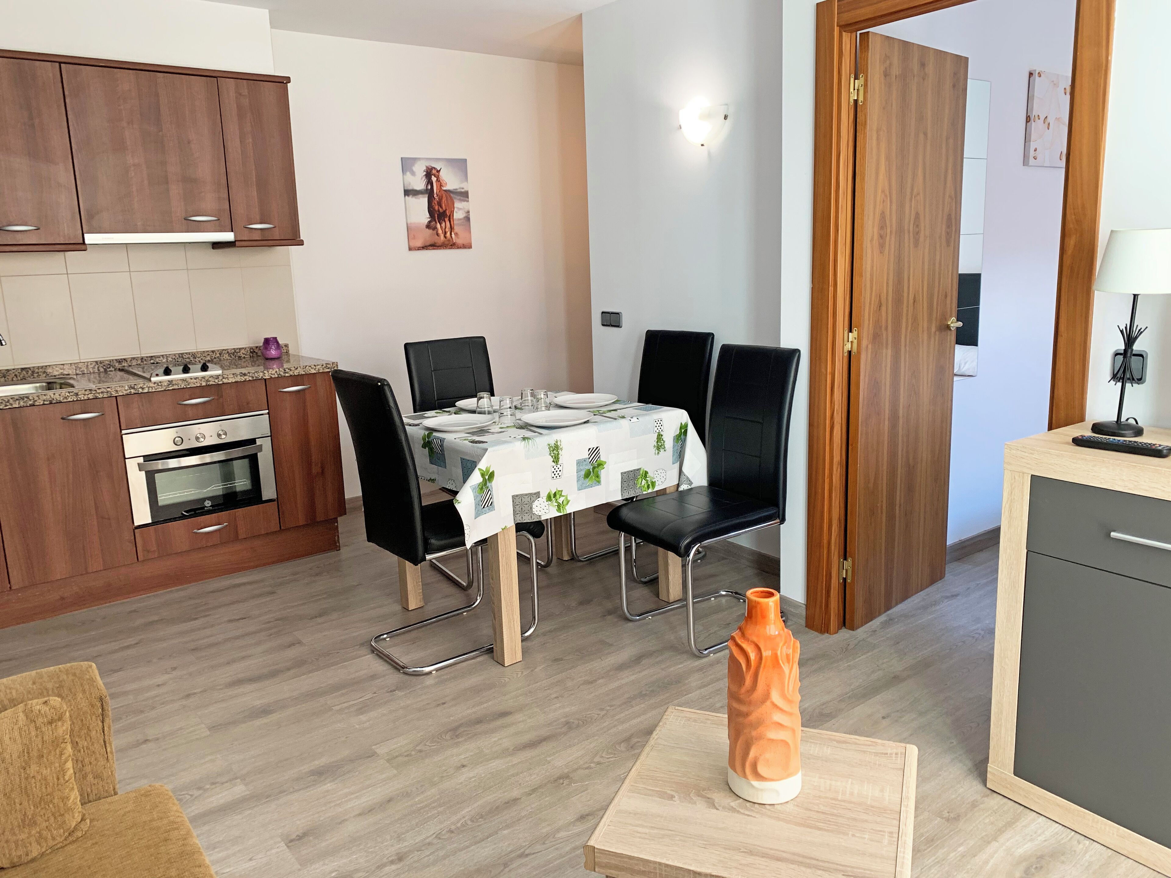A modern kitchen with wooden cabinets, a built-in oven, and a dining area with a table set for two.