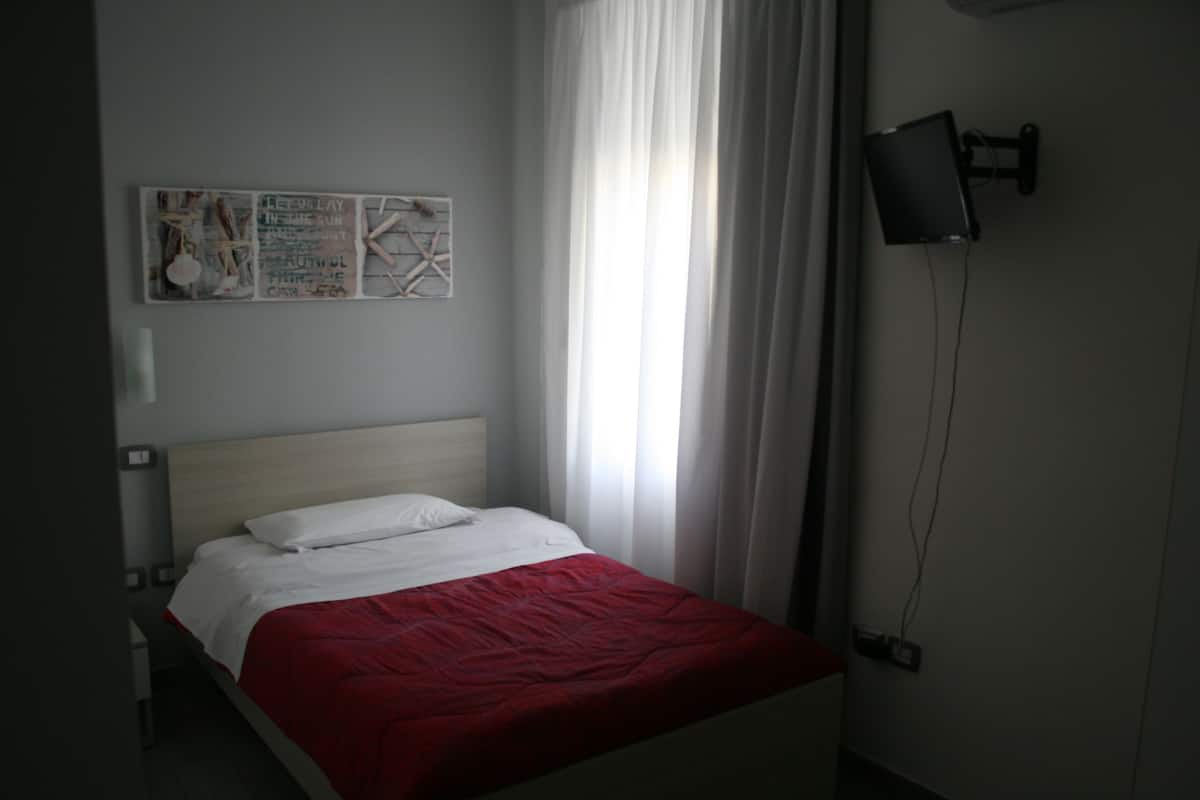 A bedroom with a bed, a wall-mounted TV, and a window with curtains.