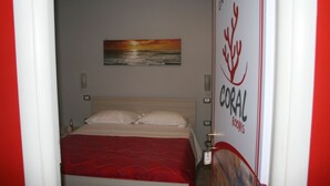 Een hotelkamer met een bed, een schilderij van een zonsondergang en een deur met een bordje in een koraalthema.