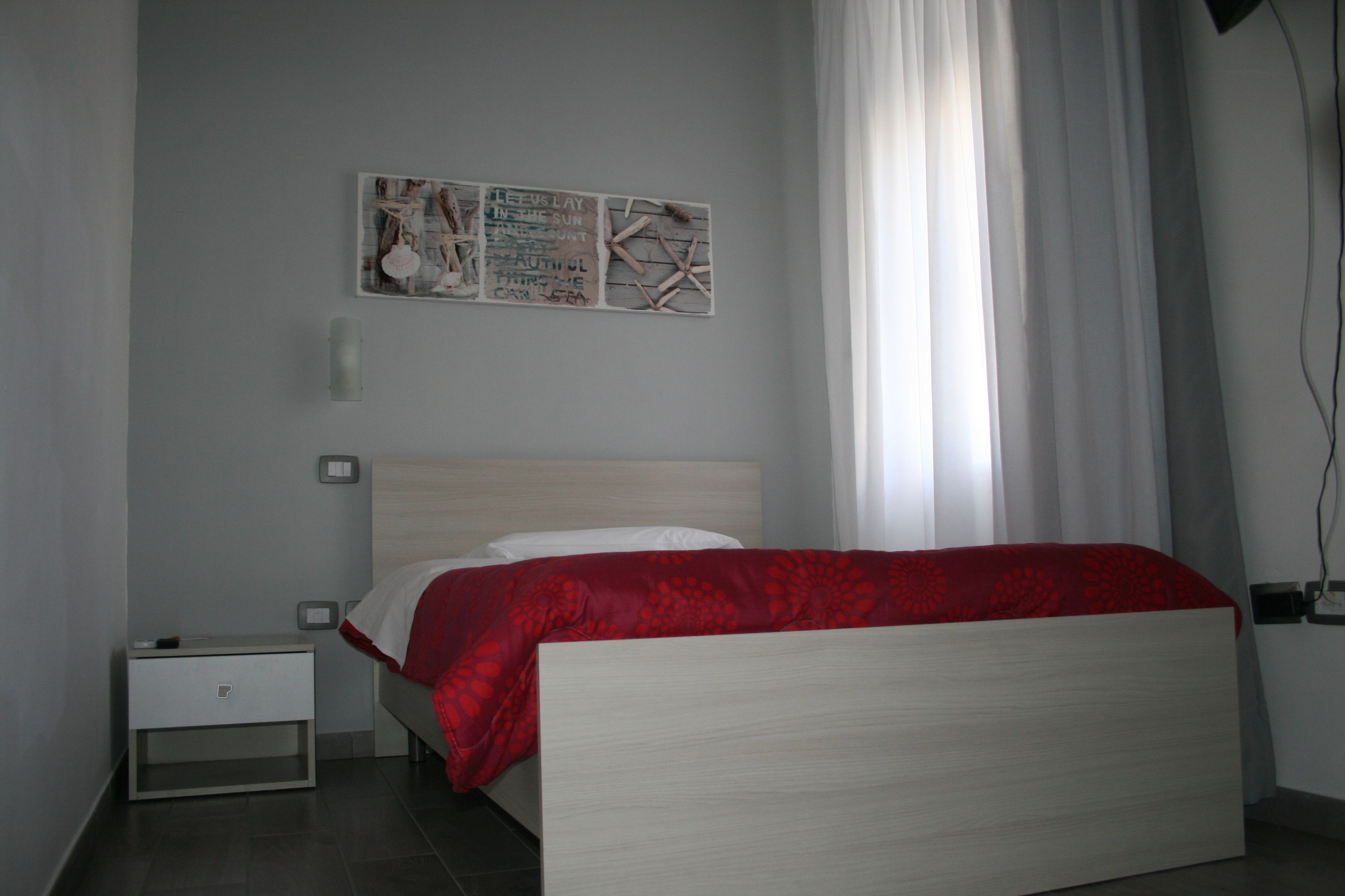 A bedroom with a bed, a nightstand, a wall-mounted light, and a window with curtains.