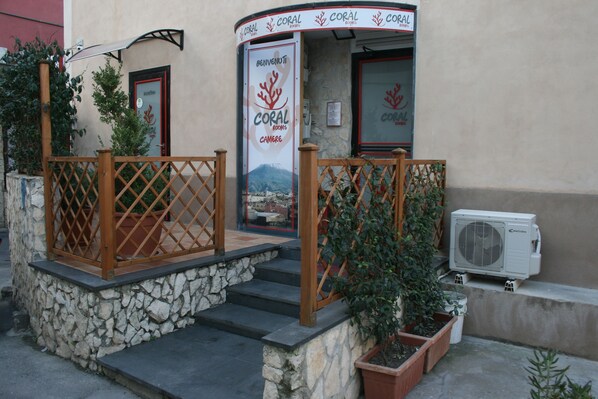 Entrada de un hotel con una escalera de piedra, barandillas de madera y un letrero que dice 'Coral Rooms'.