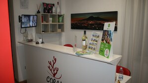 Een receptiebalie met een 'CORAL ROOMS' logo, een televisiescherm, een stadsbeeld in een lijst en een waterfles.