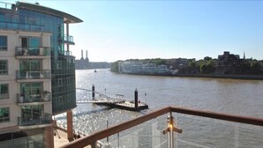 A river view from a building with a glass balcony, a bridge, and a distant cityscape. - NG Apartments London (London)