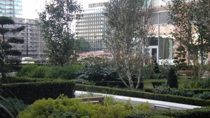 A landscaped garden with neatly trimmed hedges and trees, a bench, and a building with a modern design in the background. - NG Apartments London (London)