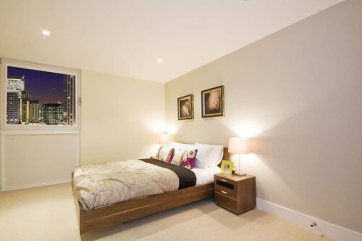 A bedroom with a city view, a bed, bedside lamps, and two framed pictures on the wall.