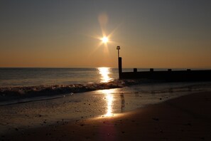 A beach scene with the sun setting over the ocean, a pier extending into the water, and footprints on the wet sand. - Hotel 50 (Bournemouth)
