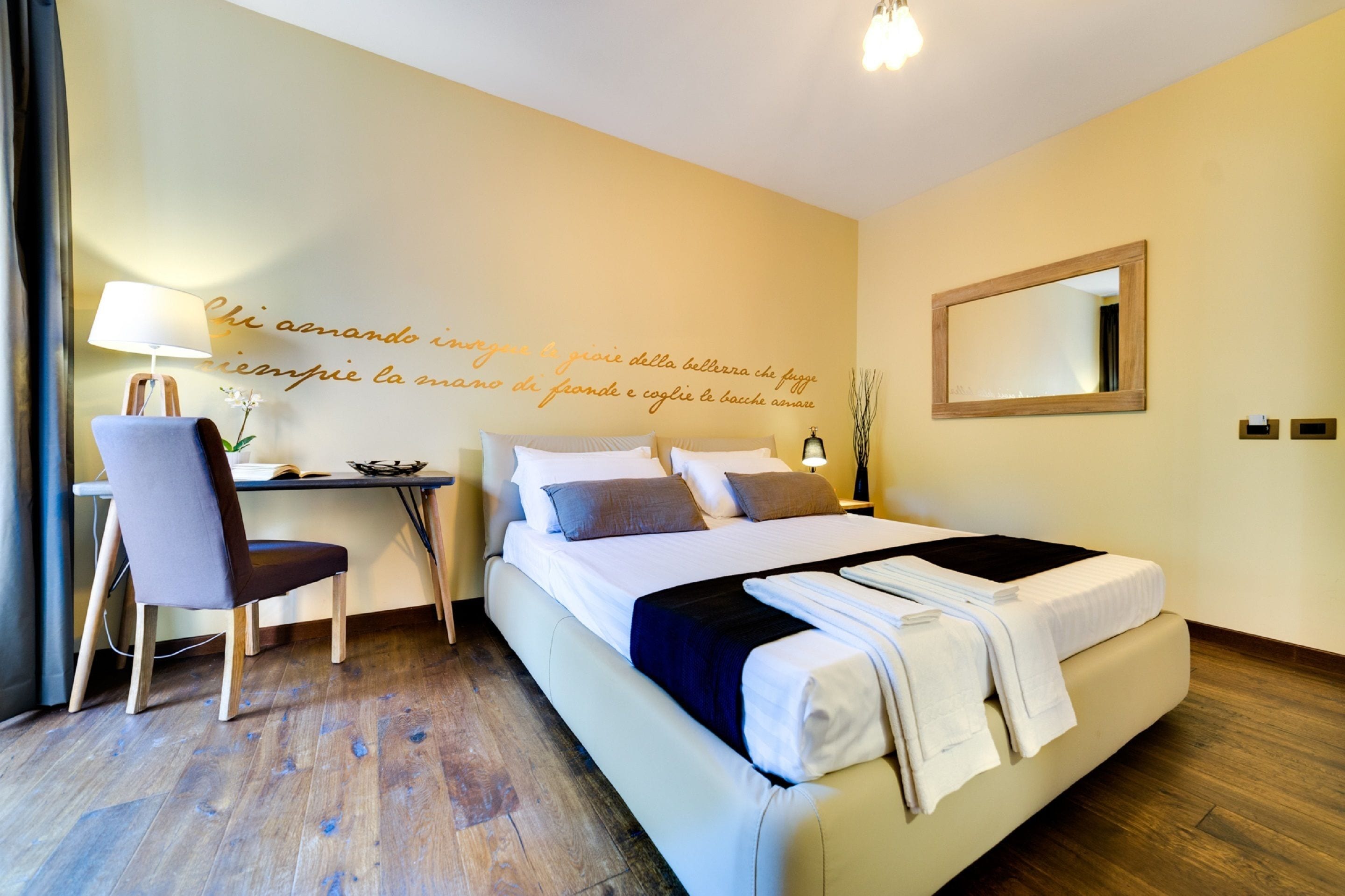 Une chambre d’hôtel équipée d’un lit, d’un bureau, d’une chaise et d’un mur orné d’une citation décorative.