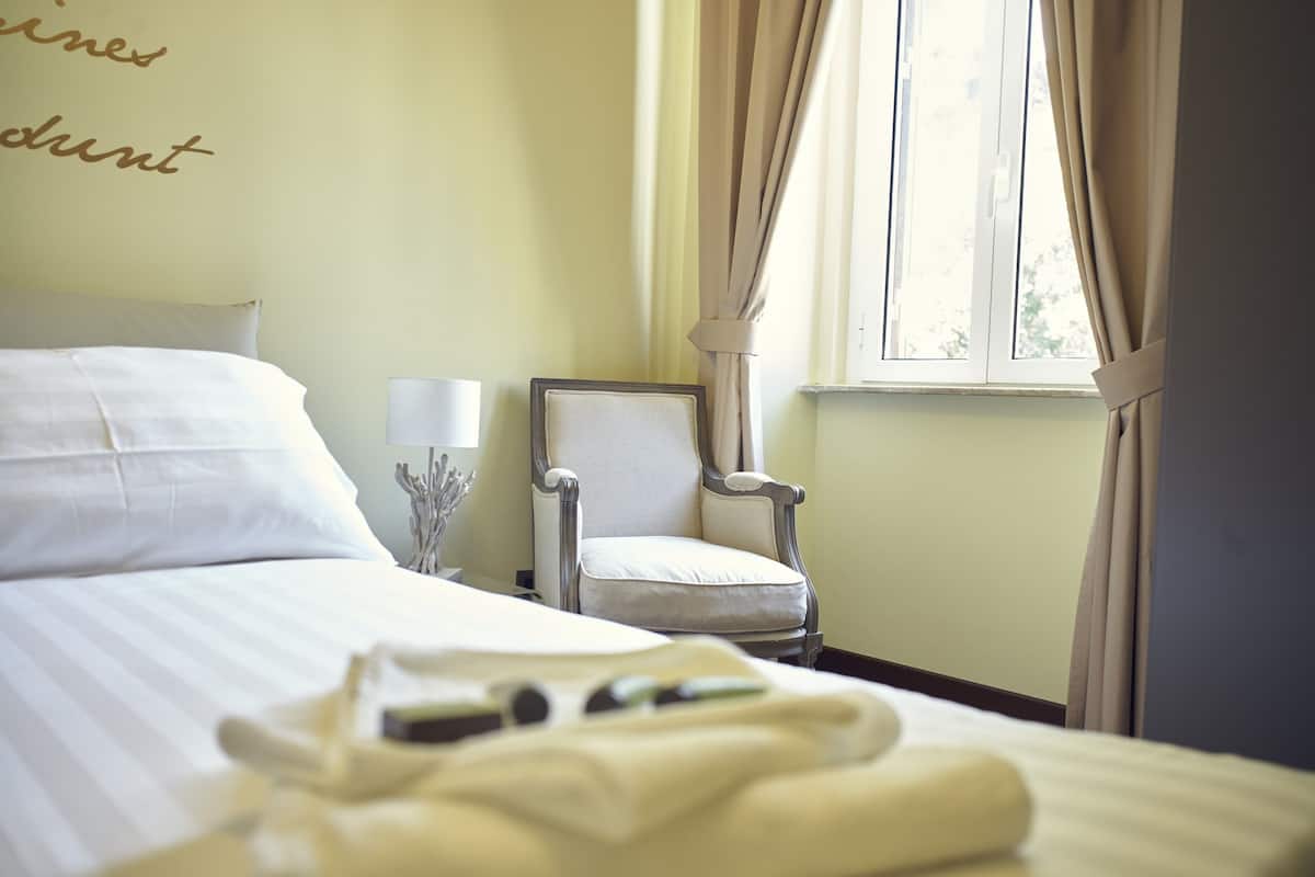 A neatly made bed with white linens, a chair with a cushion, and a window with curtains.