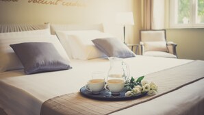 Een netjes opgemaakt bed met kussens, een dienblad met twee kopjes thee, een kan en een bloemenboeket.