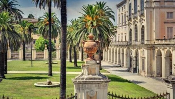 Een binnenplaats met palmbomen, een fontein en klassieke architectuur.