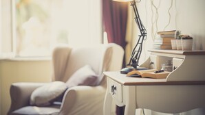 Een werkruimte met een bureau, boeken, een lamp en een raam met gordijnen.
